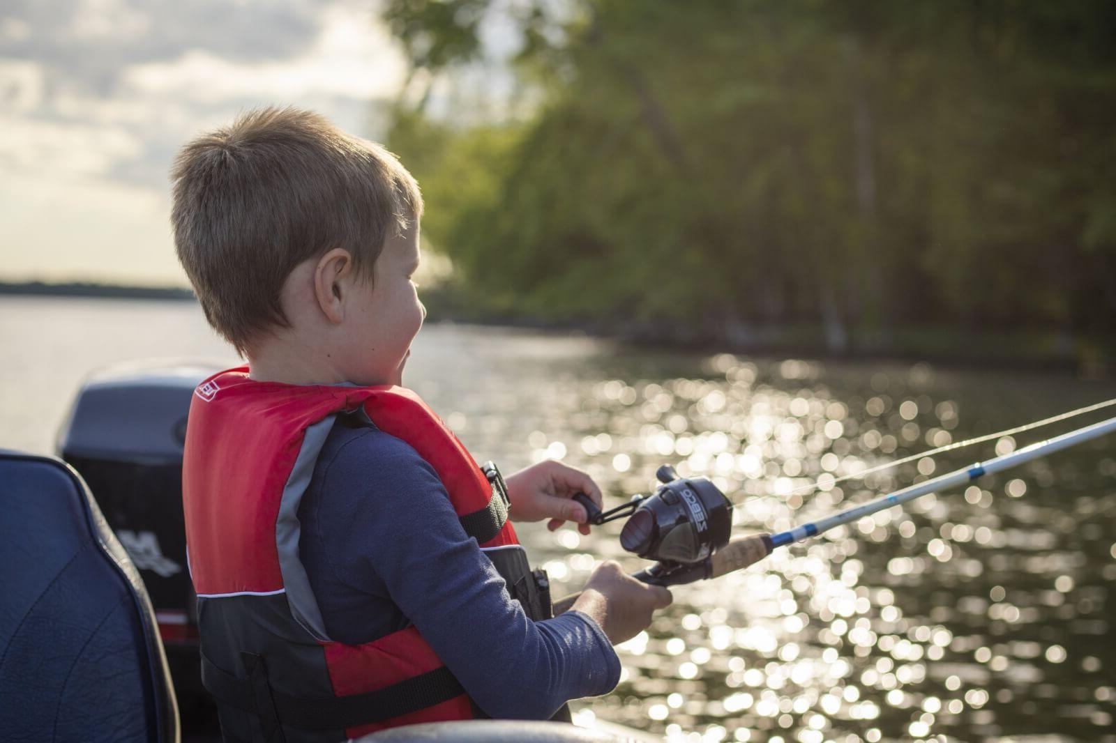 Young boy in a red vest  holding a fishing rod and Fashioning on a lake